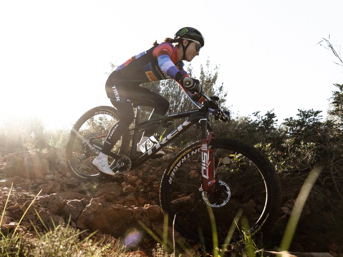Cyclist wearing helmet while riding all-new Top Fuel 9.9 RSL mountain bike down rocky trail with sun shining in background
