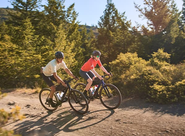 Lifestyle shot of two cyclists wearing helmets and sunglasses on gravel bikes