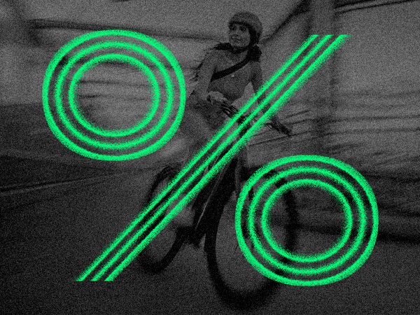 A person rides a bicycle in motion blur with a large green percentage symbol overlaying the image