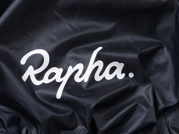Close-up of dark fabric with the 'Rapha' logo in large, white script lettering.