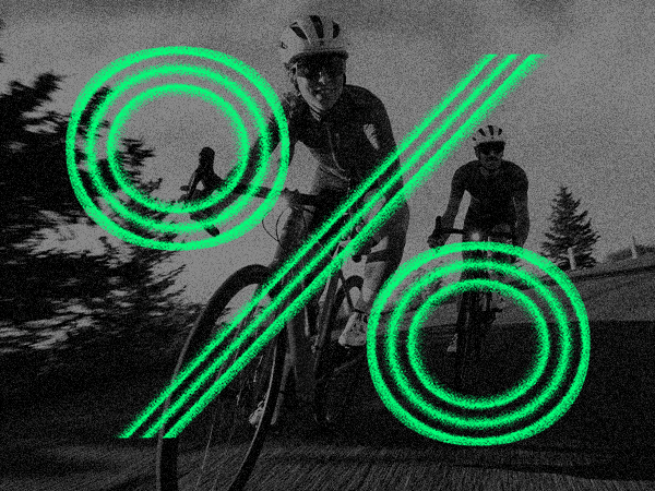 Two people ride bicycles in motion blur with a large green percentage symbol overlaying the image