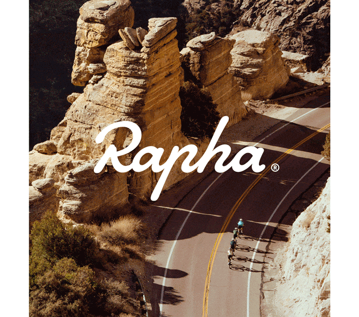 Rapha logo overlaying image of cyclists wearing helmets while riding bikes on paved road with rock formations in background