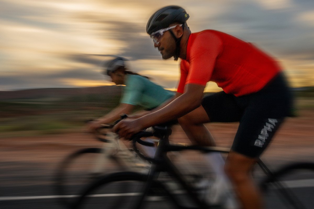 Cyclists wearing helmets and sunglasses while riding bikes on paved road with trees in background