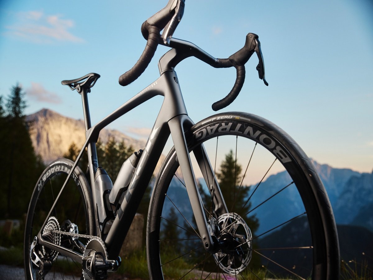Two cyclists cycling outdoors nature scenic landscape hills mountains trees grass sky sunny day summer spring
