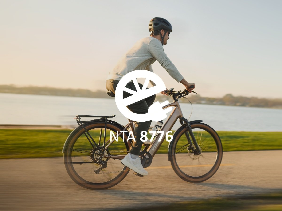 A cyclist riding an e-bike along a waterfront path, with an NTA 8776 e-bike certification badge overlay