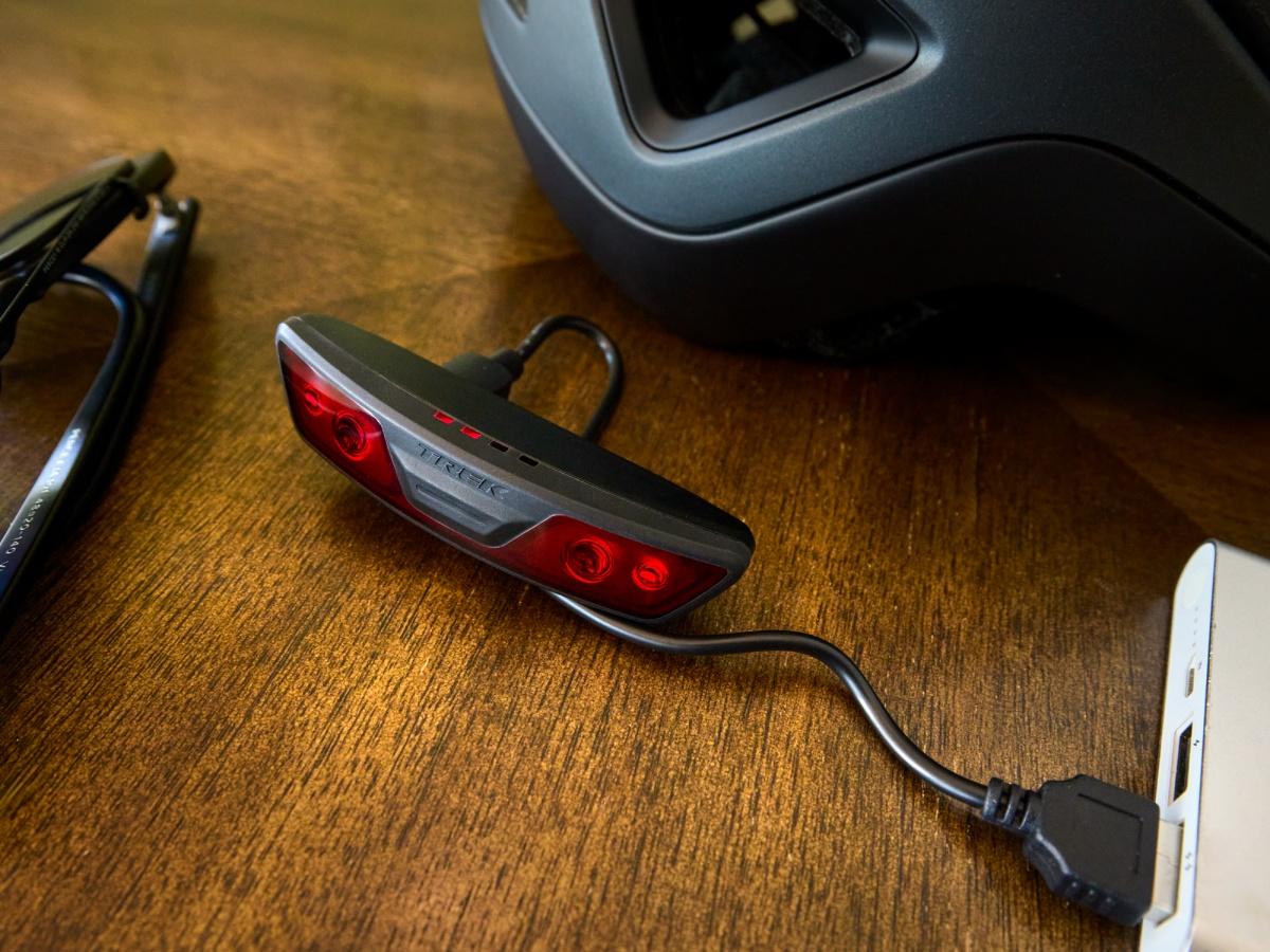 The Trek Charge WaveCel helmet's rear light charging via USB-C cable on a wooden table