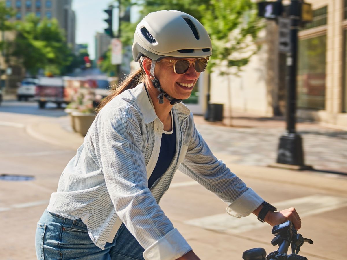 A smiling woman wearing the Trek Charge WaveCel helmet while riding through a city street
