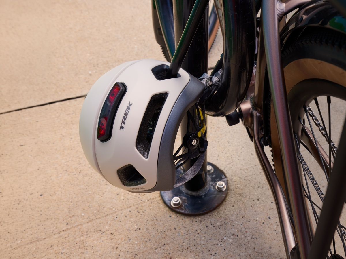 The Trek Charge WaveCel helmet locked to a bike rack, showing its USB-C charging port and lock vent