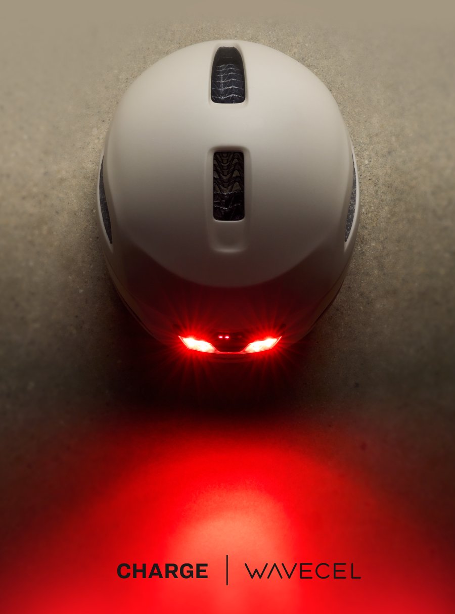 Top-down view of the Trek Charge WaveCel helmet's integrated rear light, glowing red and transitioning into a Charge WaveCel wordmark lockup