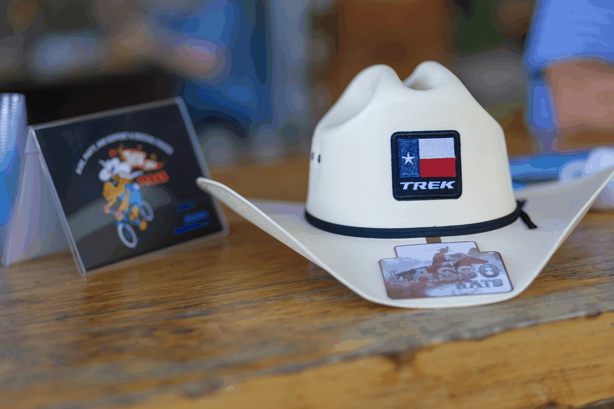 Slideshow of Trek 100 Texas event moments: a Trek cowboy hat on display, riders shaking hands, and a group celebrating in Trek cowboy hats