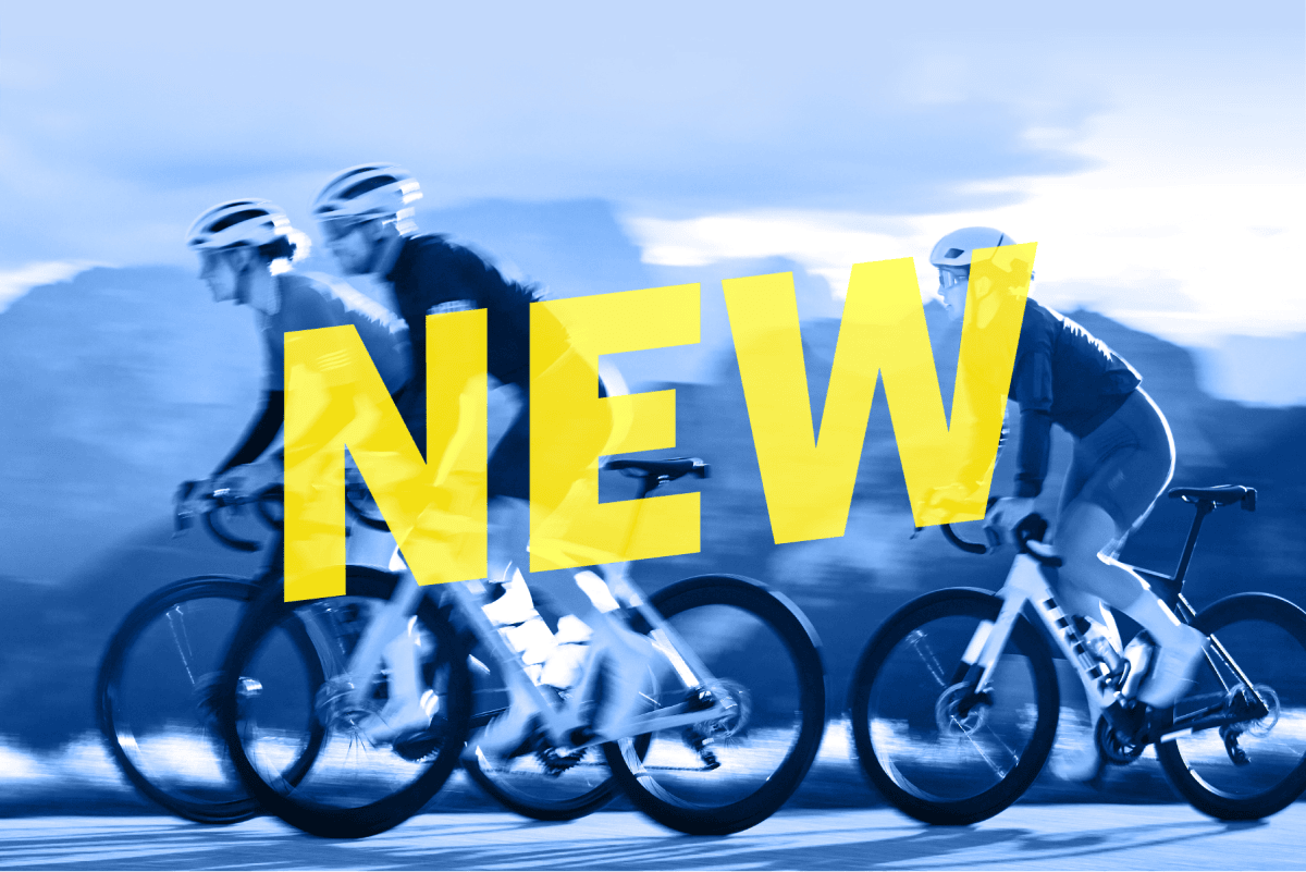 The word 'NEW' overlaying image of cyclists wearing helmets while riding bikes on paved road with mountains in background