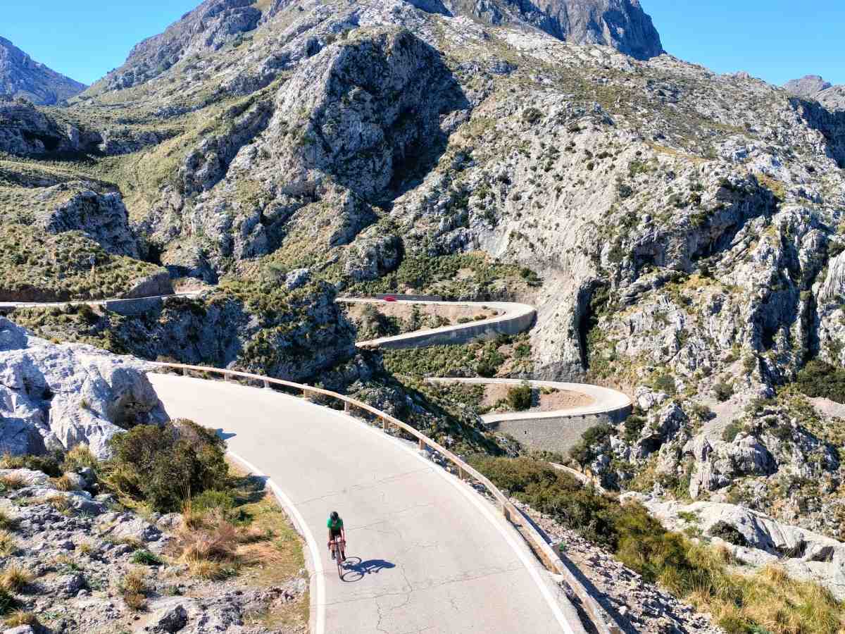 A cyclist climbing a winding switchback road through Mallorca's limestone mountains