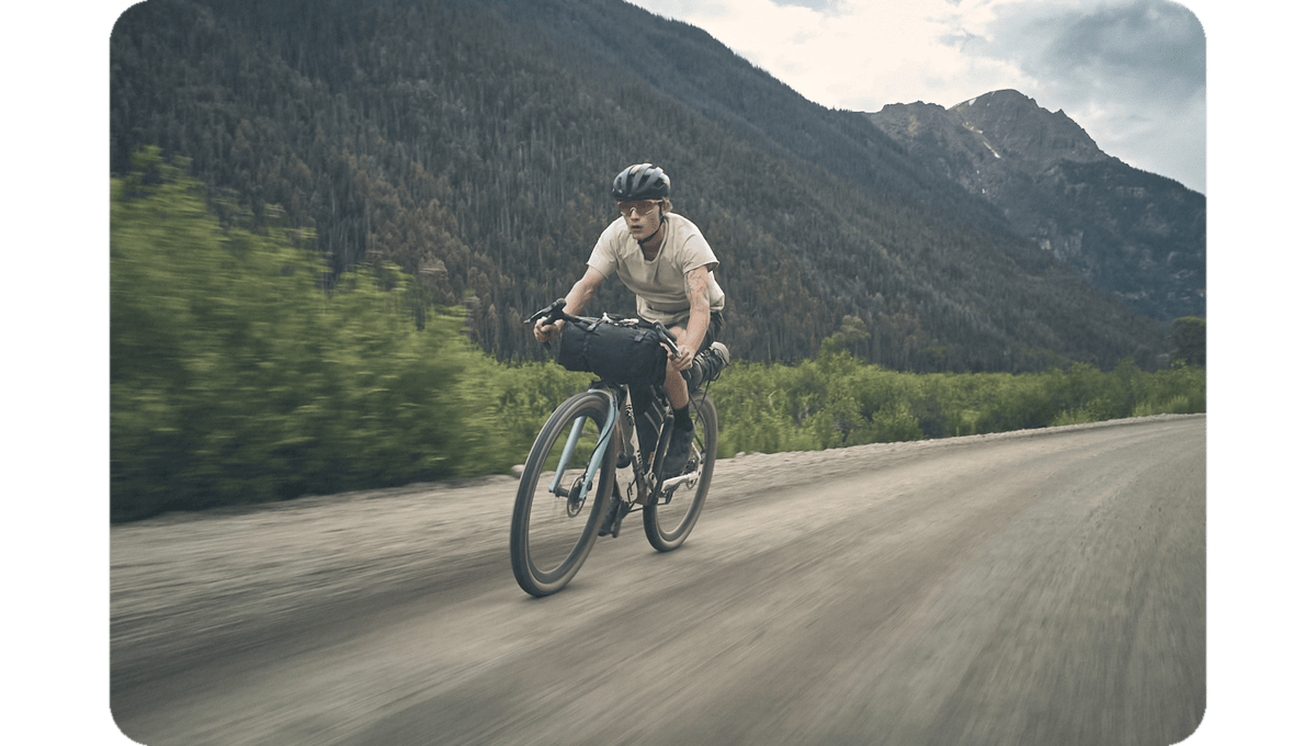 Cyclist riding a gravel bike on a paved mountain road with trees behind